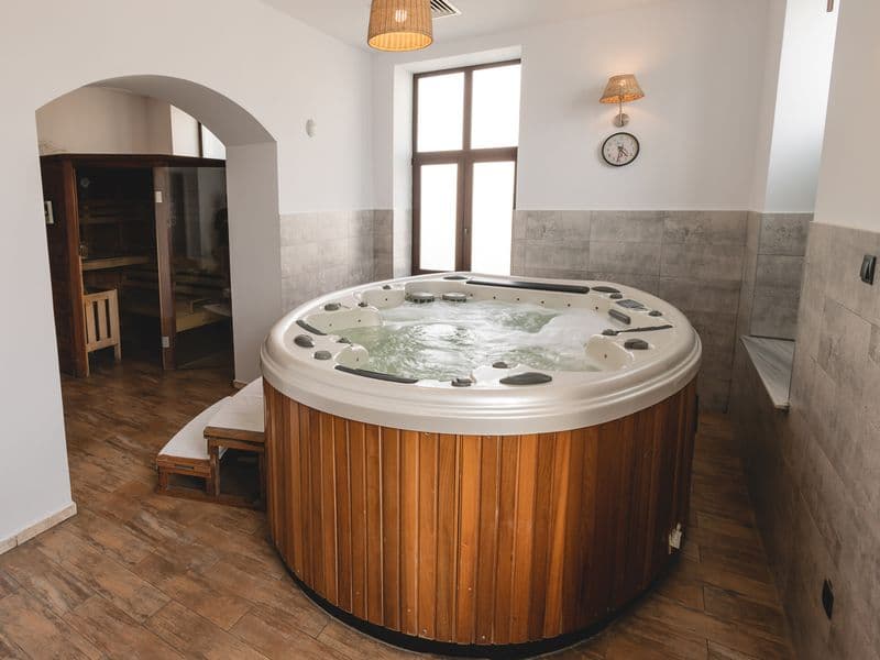 Jacuzzi rotund cu margine de lemn în spa-ul Hotelului Carol, cu ferestre înalte și ușa saunei în fundal