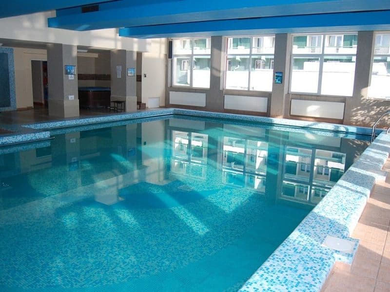 Piscina interioară a Complexului Bradul-Călimani, cu apă albastră, margine de mozaic și ferestre pe toată lungimea