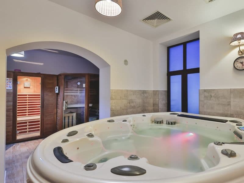 Centrul spa al Hotelului Carol: jacuzzi rotund alb sub o arcadă, cu sauna cu infraroșu în încăperea alăturată
